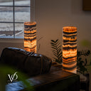 Illuminated Tangerine Onyx lamp pair viewed across a leather sofa, with a window, greenery and books in the setting.