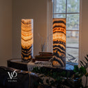 Angled view of illuminated Tangerine Onyx lamps on a console, with the right lamp in the foreground beside books and a cream throw.