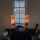 Wide front view of illuminated Tangerine Onyx lamps flanking books and a small vase on a console beneath a tall window.