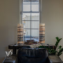 Wide unlit view of Tangerine Onyx lamps with cream, peach, gray, and brown layers, styled with books and a cream throw behind a leather sofa.