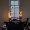 Rotated view of glowing Tangerine Onyx lamps, with curled dark markings near the left rim and a pale formation in the right lamp’s upper bands.