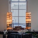 Illuminated Tangerine Onyx lamp pair with broad amber crystal bands, charcoal ribbons, and dark mottling across the lower sections.