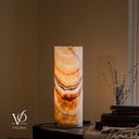 Illuminated Aqua Onyx cylinder table lamp with warm amber crystal formations, curved gray and rose bands, and an irregular rim.