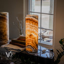 Angled view of the illuminated right Aqua Onyx lamp, showing its smooth rim and amber crystals, with its companion partly visible.