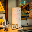 Decorative lamp with marble pattern on a table, surrounded by framed pictures and a skull in a colorful frame.