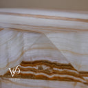 Close-up of polished geometric facets and layered honey-gold veining on the illuminated White Ice Onyx table.