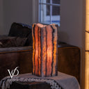 Rosa Onyx table lamp lit from within with dramatic vertical mineral patterns and a natural live-edge top