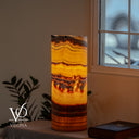 Illuminated Miami Sunset Onyx live-edge cylinder lamp glowing with golden orange, amber, red, and dark brown banding