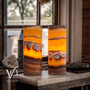 Two tall cylindrical lamps made from polished agate with vibrant orange, yellow, and brown banding, displayed on a stone table in a rustic room setting.