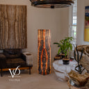 Wide room view of the glowing Tangerine Onyx floor lamp beside a leather chair, potted plants, and a white stone table.