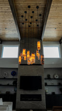 Modern glass tube chandelier with warm yellow light, dark metal frame and hanging wires.