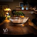 Decorative bowl with a plant on a wooden table in a softly lit room.