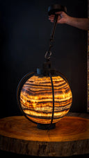 Warm, amber-hued onyx globe pendant light with a dark metal frame and chain.