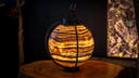 A warm, glowing spherical pendant lamp crafted from layered orange and brown onyx stone with a black metal frame.